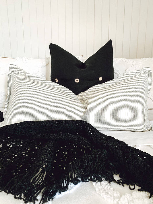 Bed with linen strip and black cushion with black knitted throw